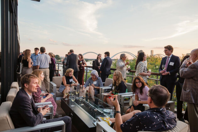 A group of people sitting on the outside terrace of District Winery with the Anacostia Bridge in the background during sunset.
