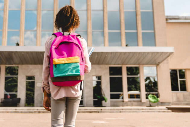 Girl with backpack looking at school building.