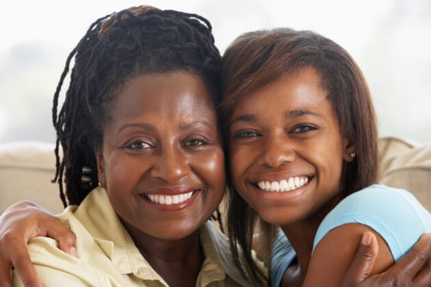 Mother and teen daughter hugging and smiling at the camera.