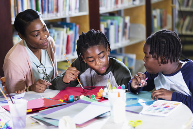 Two African-American boys sitting at a table in the library with their mother.