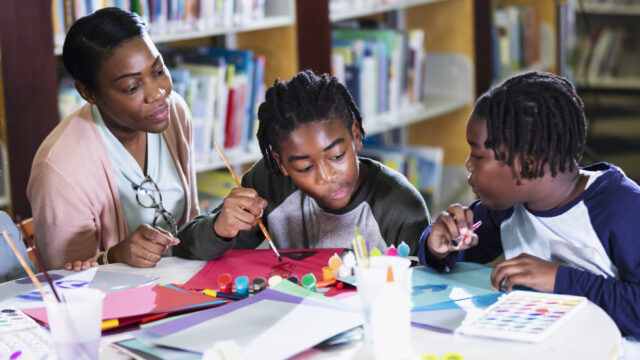 Two African-American boys sitting at a table in the library with their mother.