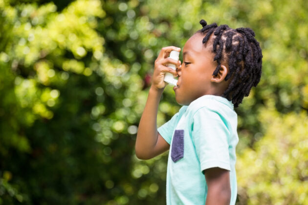 Photo of side profile of boy using an asthma inhaler in a park.